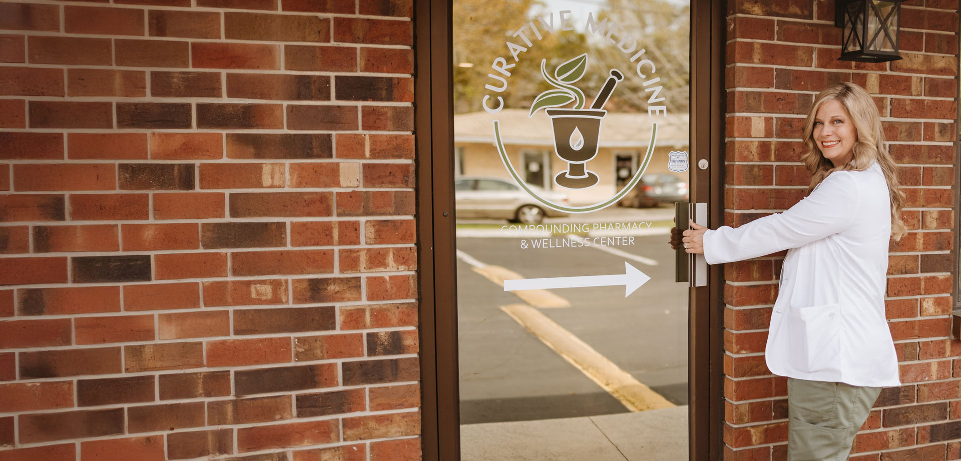 Dr. Jennifer Bennett, PharmD, opening the glass door at Curative Medicine compounding pharmacy in Gainesville