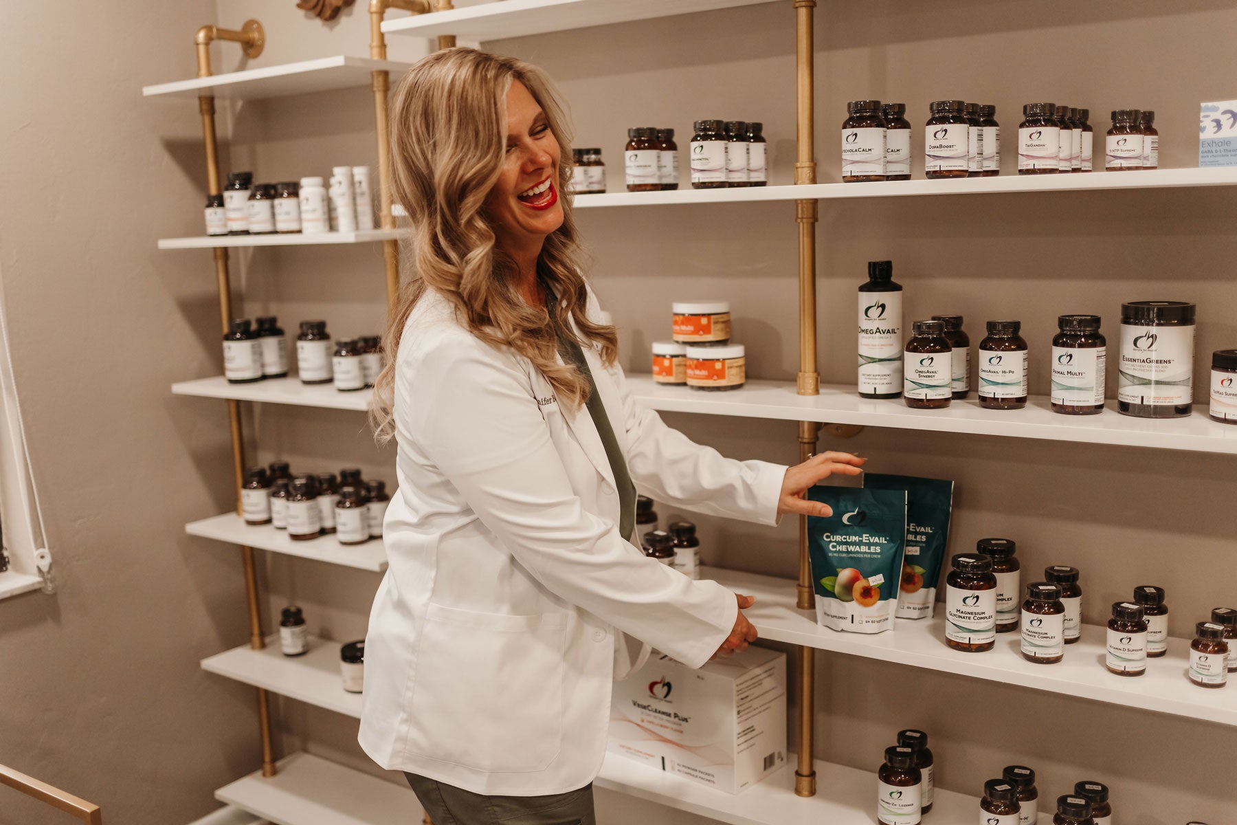 Dr. Jennifer Bennett laughing while stocking wellness shelves at Curative Medicine
